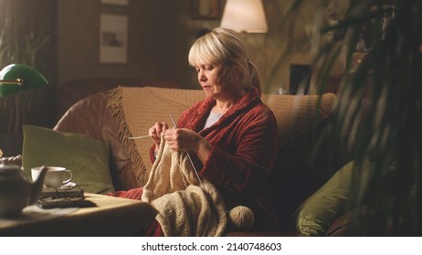 A retired woman knitting a warm sweater at her leisure time while sitting on the sofa in the evening near her husband with newspaper - Powered by Shutterstock