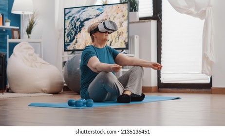 Retired Woman Meditating In Lotus Position With Vr Glasses On Yoga Mat. Pensioner Using Virtual Reality Headset And Doing Meditation To Relax. Senior Person Wearing Goggles To Meditate.