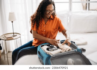 Retired woman organising her luggage for a stay at a luxurious hotel. Mature woman sitting on a bed, surrounded by her travel essentials, and smiling as she packs her suitcase for a bucket list trip. - Powered by Shutterstock