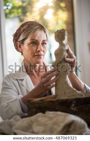a retired woman is passionate about sculpture, she is in her atelier. she is happy of her work, she is concentrated, she is sculpting a woman. the statue is at foreground
