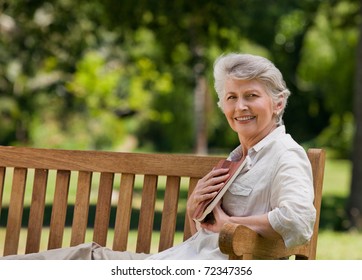Retired Woman Reading A Book On The  Bench