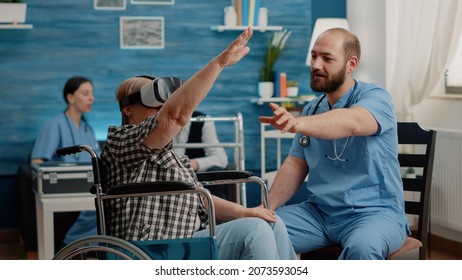 Retired woman using vr glasses and nurse assisting, explaining virtual reality in nursing facility. Senior patient sitting in wheelchair wearing headset at checkup with medical specialist - Powered by Shutterstock
