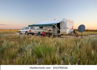 Retiree Sitting Under Awning Of Caravan With Four Wheel Drive Vehicle At Sunset.