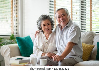 Retirement Asian Elderly Chinese Couple enjoying life in the home. Happy smiling Senior man and woman sitting in couch. Portrait of Older family looking at camera.
