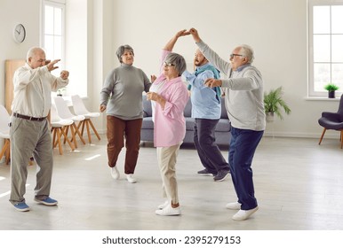 Retirement community. Elderly men and women actively spend time having fun and dancing at party in nursing home. Group of senior Caucasian people laughing and dancing together in living room. - Powered by Shutterstock