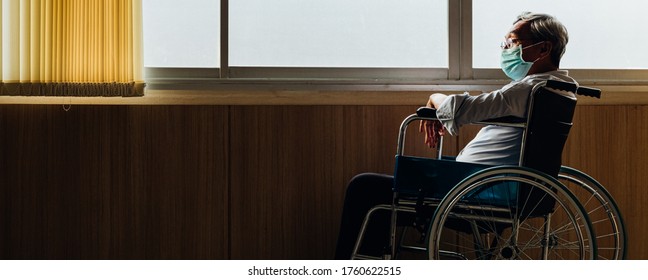 Retirement concept. Panoramic asian elderly man wear mask sitting in wheelchair while looking out the window in nursing home or hospital.