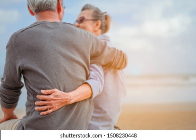 Retirement couple sitting by the sea, women embrace husbands and look at each other at the beach in the morning, life insurance plan at the retirement concept.
