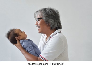 Retirement Grandpa So Happy To Holding Thai Grandchild Baby Boy In His Arms, Looking At Adorable Baby With Love. Backgorund- Copy Space