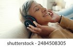 Retirement, mature woman and sofa with headphones, relax and calm in living room, streaming music and audio. Rest, happy and senior lady with headset for podcast, radio and carefree on couch