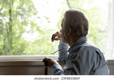 Retirement problem. Pensive old man nursing home patient sit by window hold glasses walking stick lost in sad thoughts. Upset aged male think about bad health loneliness miss deceased wife. Copy space - Powered by Shutterstock