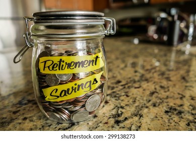 Retirement Savings Money Jar. A Clear Glass Jar Filed With Coins And Bills, Saving Money. The Words 