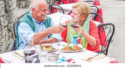 Retirement senior couple drinking and eating in restaurant outdoor - Mature husband and wife having fun in romantic vacation - Love, relationship and joyful elderly lifestyle concept