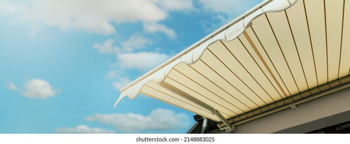 retractable awning installed on wall over house window against blue sky. banner with copy space - Shutterstock ID 2148883025