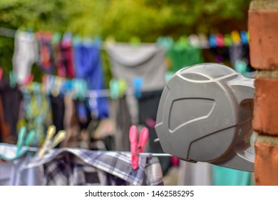 Retractable Washing Line Fixed At Brick Wall Background Blurred Row Of Colorful  Clothes And Pegs Hanging On The Line And Natural Green. Concept Drying Clothes Outside In Sunshine.