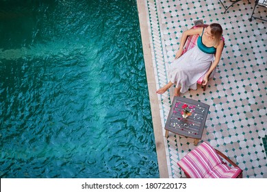 Retreat And Vacation. Beautiful Young Woman Relaxing Near Spa Private Swimming Pool In Beautiful Moroccan Backyard.