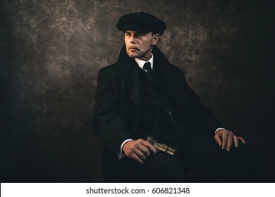 Retro 1920s english gangster with gun sitting on chair. Peaky blinders style.