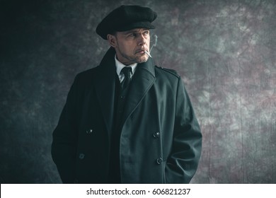 Retro 1920s english gangster smoking cigarette. Wearing black coat and flat cap.