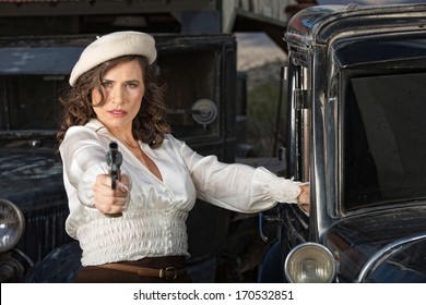 Retro 1920s era female gangster aiming gun next to car