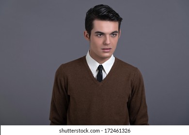 Retro 1950s Fashion Man With Dark Grease Hair. Wearing Brown Sweater With Black Tie. Studio Shot Against Grey.
