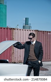 Retro 60s Mafia Business Man With Suit And Black Sunglasses Looking In Trunk Of Classic Car.