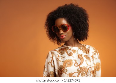 Retro 70s Fashion African Woman With Paisley Dress And Sunglasses. Brown Background.