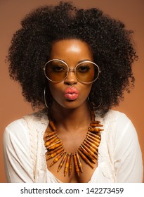 Retro 70s Fashion Black Woman With Sunglasses And White Shirt. Brown Background.