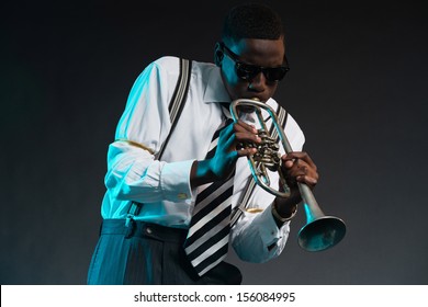 Retro african american jazz musician playing on his trumpet. Wearing shirt and tie and sunglasses. Studio shot.
