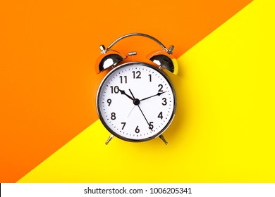 Retro alarm clock on half orange and yellow background