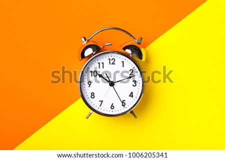 Retro alarm clock on half orange and yellow background