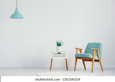 Retro-Sessel neben einem kleinen weißen Tisch mit Pflanzen in Topf in hellem Interieur, reales Foto mit Kopienraum auf der leeren Wand