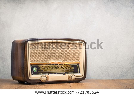 Retro broadcast radio receiver with green eye light on wooden table circa 1950 front concrete wall background. Listen music concept. Vintage instagram old style filtered photo