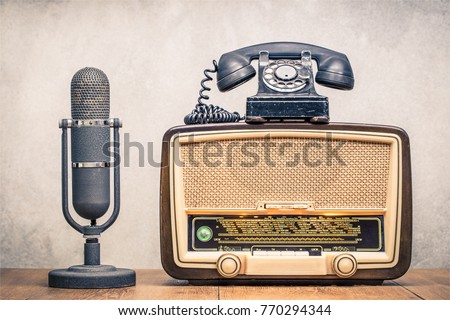 Retro broadcast table radio receiver with green eye light, studio microphone circa 1950 and telephone front concrete wall background. Listen music concept. Vintage instagram old style filtered photo