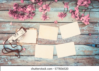 Retro camera and empty old instant paper photo album on wood table with flowers border design - concept of remembrance and nostalgia in spring. vintage style