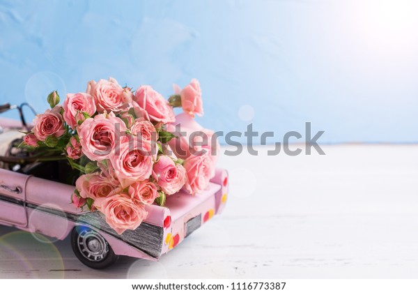 Retro car with pink\
roses flowers against blue wall. Romantic background. Selective\
focus. Place for text. 
