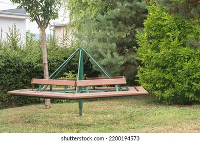 Retro Carousel For Kids Made Of Wood And Iron. Children's Roundabout Placed Home In The Backyard. Surrounded By Garden Foliage. 