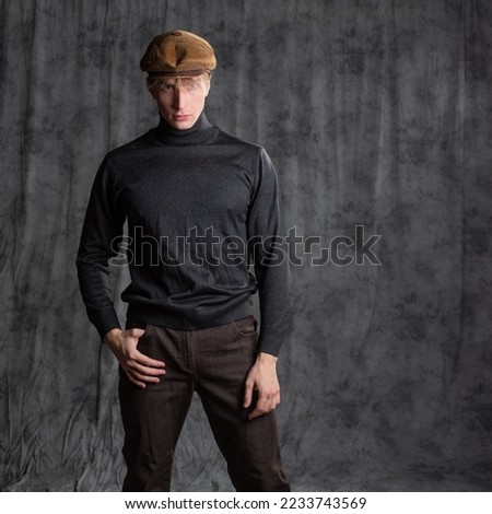 Retro character in the style of the 60s. A young man in a flat cap and a black turtleneck. Posing in the studio on a gray background