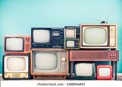 Retro classic TV receivers set from circa 60s, 70s and 80s, old wooden television stand with amplifier front mint blue wall background. Broadcasting, news concept. Vintage style filtered photo