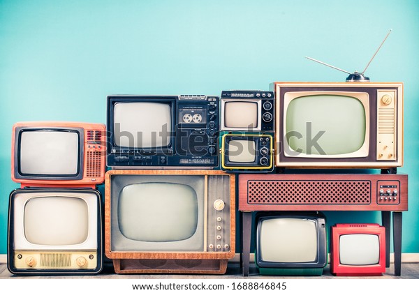 Retro classic TV receivers set from circa 60s, 70s\
and 80s, old wooden television stand with amplifier front mint blue\
wall background. Broadcasting, news concept. Vintage style filtered\
photo