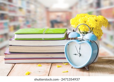 retro clock and yellow flower in white pot on wooden floor with stack books over blurred background.  - Powered by Shutterstock