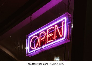 Retro club inscription Open. Vintage electric signboard with bright neon lights. Pink light falls on a brick background.