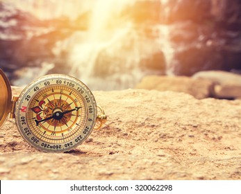 The retro compass on the rock with waterfall blurred background and sunlight. Vintage style and filtered process