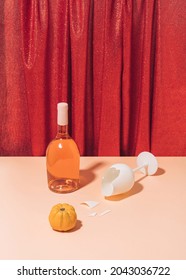 Retro Composition With Beige Table, Broken Wine Glass And Bottle Against Shiny Red Curtain. Wild Vintage Halloween Or Thanksgiving Party Concept.