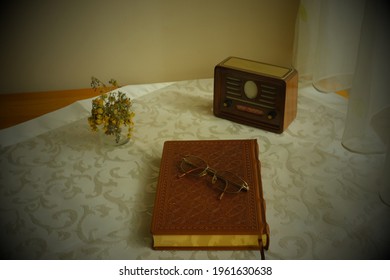 Retro concept desk with antique photo view. Nostalgic radio, glasses on a leather-covered gilded book, dried yellow flowers in a vase on a lacy table, top view. Koran, bible, new testament, holly.