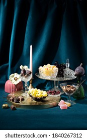 Retro concept stage made of crystal food table, snacks and sweets on navy blue velvet curtain background. Minimal art direction food decoration concept. Vintage 70s aesthetic trend.