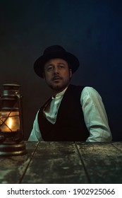 Retro cowboy victorian style man behind wooden table with historical oil lantern.