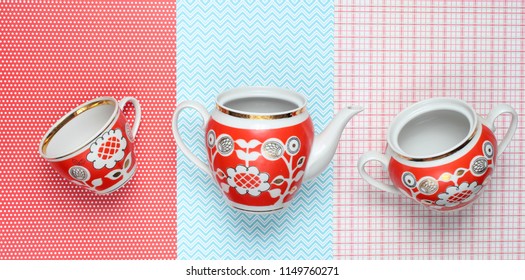 Retro cups and teapot with red patterns on tablecloth. Top view