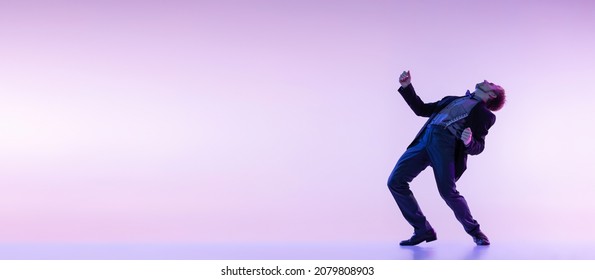 Retro Dance. Portrait Of Young Stylish Man In Vintage Style Clothes Dancing Swing Dance Isolated On Lilac Color Background In Neon Light. Timeless Traditions, 1960s Fashion Style. Concept Of Art