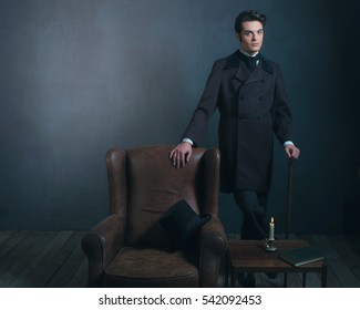 Retro dickens style man standing with cane next to leather chair.