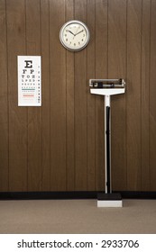 Retro Doctor's Office With Wood Paneling, Clock, Eye Chart And Scale.