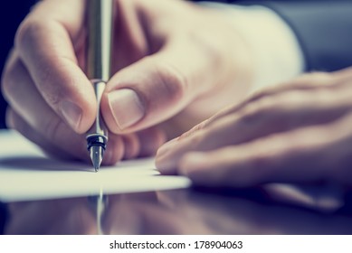 Retro Effect Faded And Toned Image Of A Man Writing A Note With A Fountain Pen.